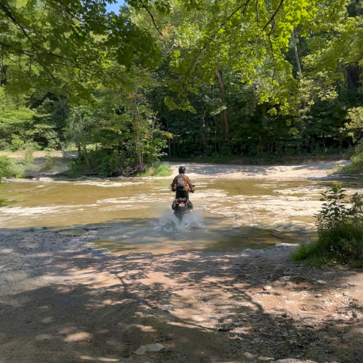 Dual sport rider crossing a creek on a trail-tested Flexi Fender kit